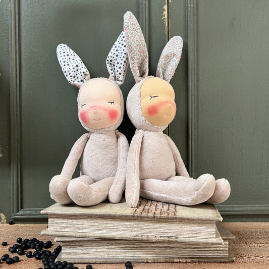 Two plush bunny toys with printed fabric ears on a stack of books against a green wall.