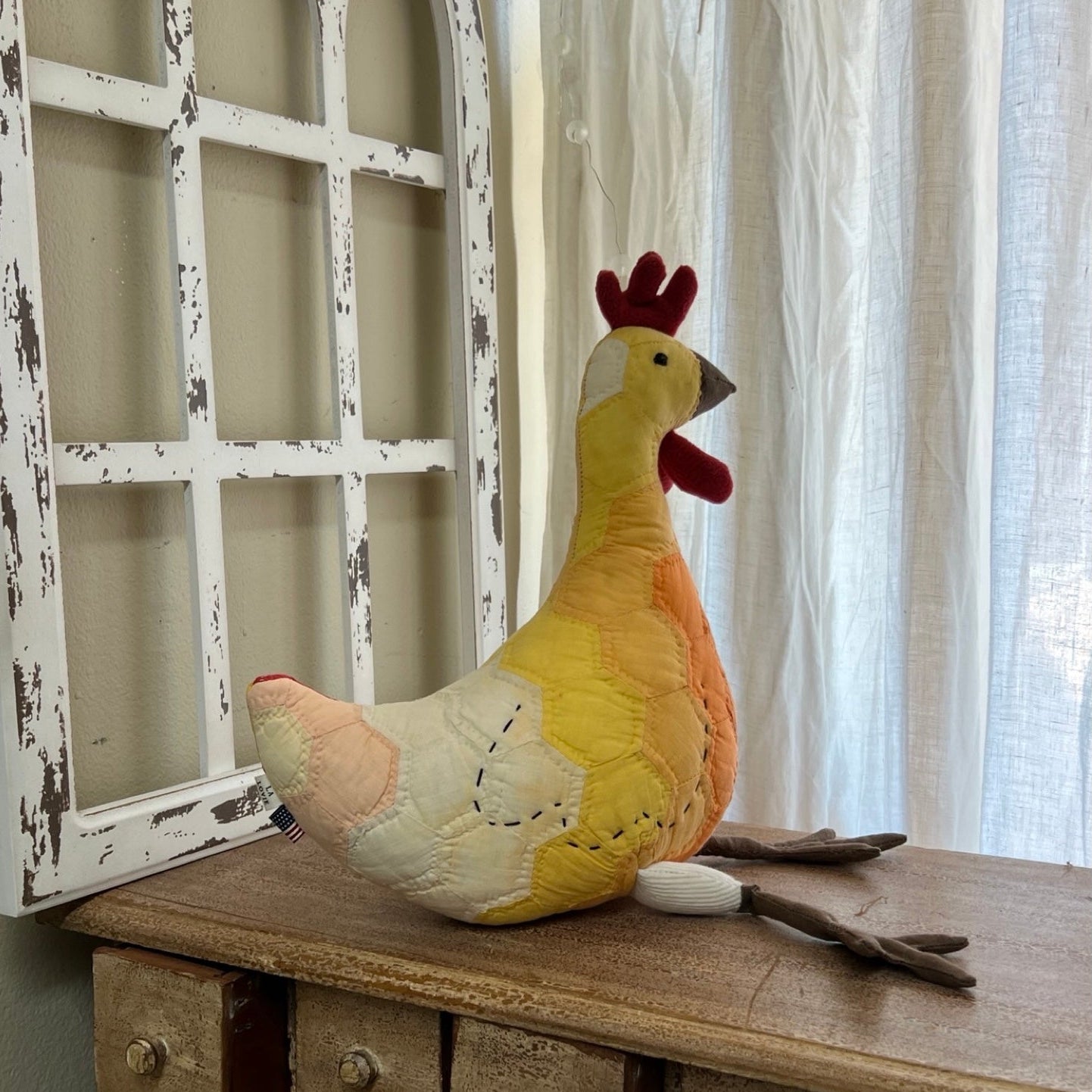 Plush chicken toy on a wooden surface with a window and curtain in the background